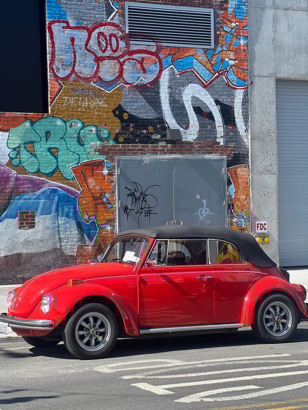 Red VW Beetle parked beside graffitied building in NYC