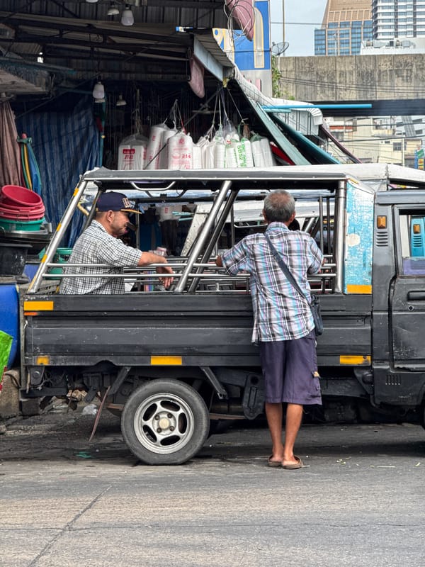 Two men ride songthaew taxi near Bangkok market