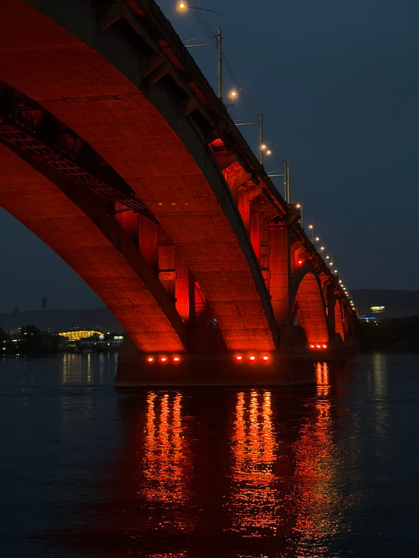 Red-lit bridges illuminate Yenisei River at dusk in Krasnoyarsk