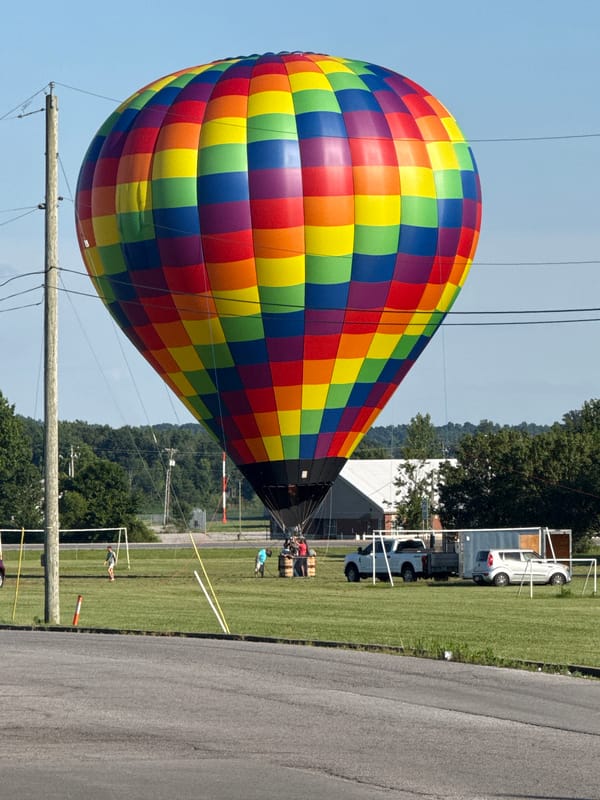 Rainbow hot air balloon lifts off from a Powderly field
