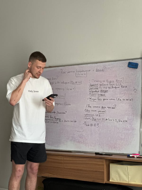 Man with religious shirt stands near Cyrillic whiteboard in Kerobokan