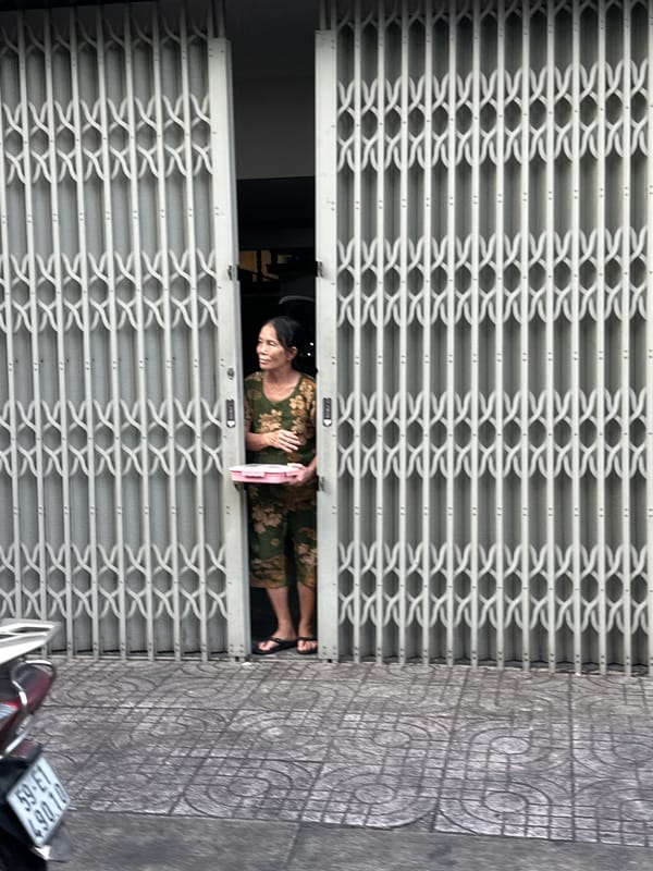 Man sits on parked moped near grid door in Thủ Đức