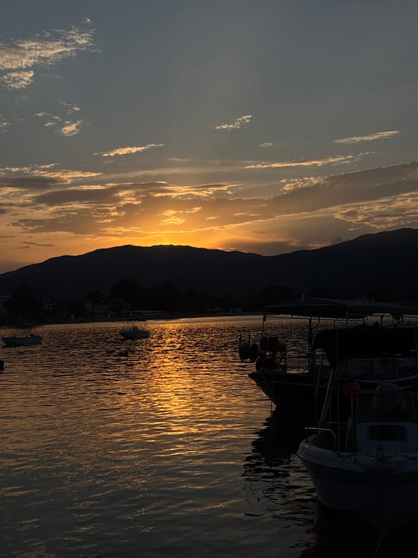Sunset over a calm harbor with boats and silhouetted hills