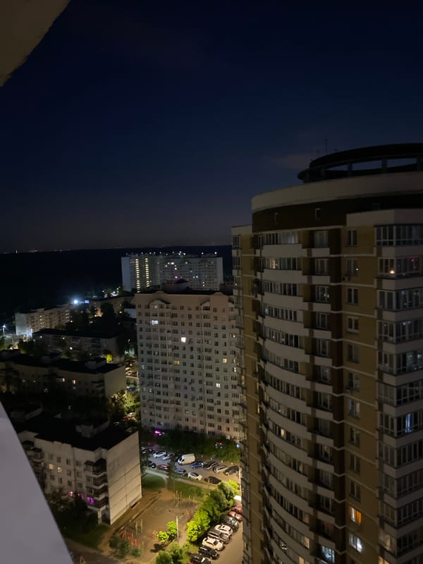 Noctilucent clouds drift over a lit residential skyline at night.