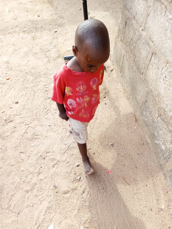 Child stands barefoot on sandy ground near textured wall