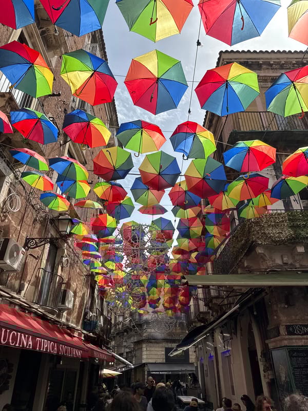 Colorful umbrellas suspended over Catania street scene observed