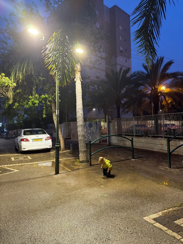 Child plays in wet Kiryat Bialik square at dusk
