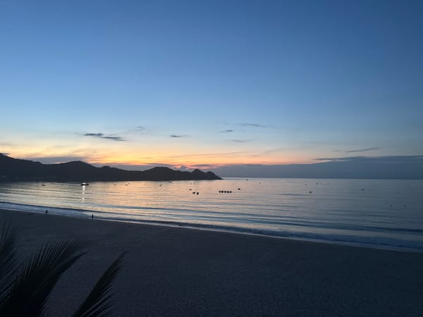 Calm beach at dusk, boats on the water, sky on fire