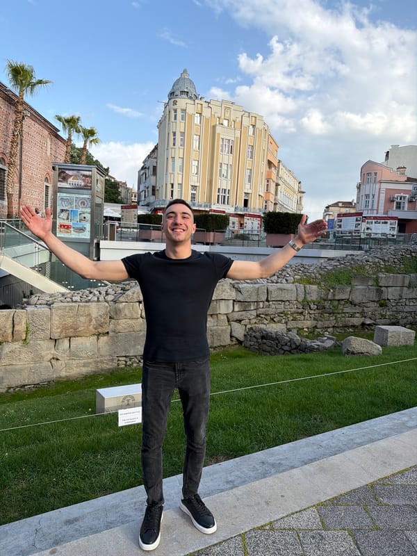 Man stands with arms outstretched, smiling in urban setting
