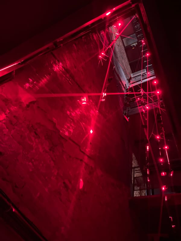 Red-lit installation space with lasers, crowds, and theatrical projections