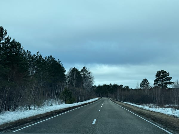 Vehicle travels winter road through forested mountainous terrain