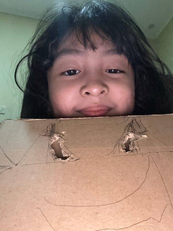 Person crafts cardboard mask, rests indoors during afternoon session