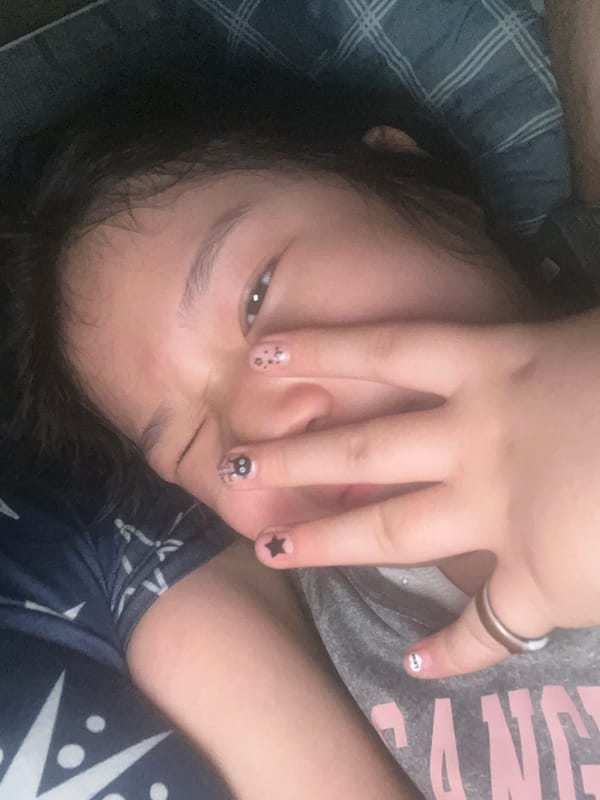 Person with decorated nails rests on plaid bed