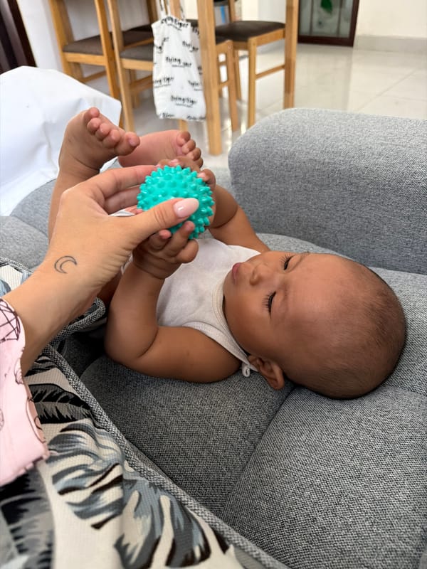 Baby and Pomeranian share a couch with a teal spiky ball
