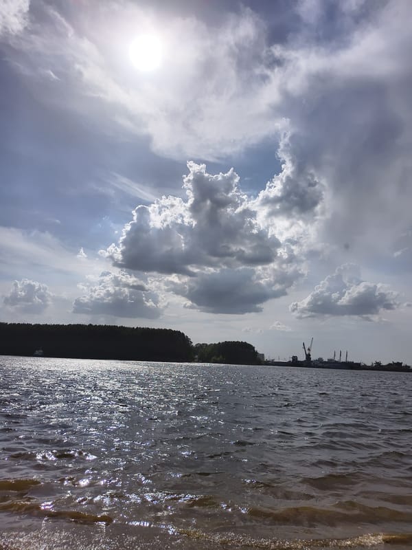 Beach day captured near industrial waterfront with passing riverboat