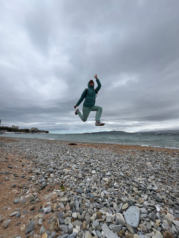Person jumps on pebble beach in green tracksuit