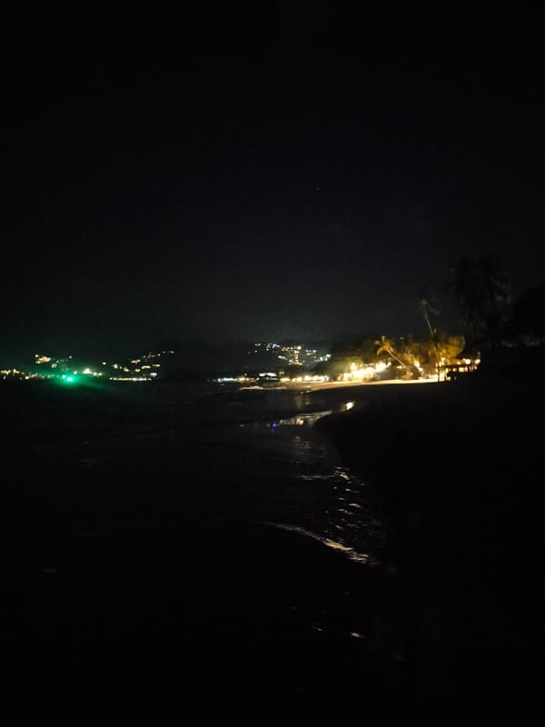 Child walks nighttime Chaweng Beach amid illuminated tropical coastline