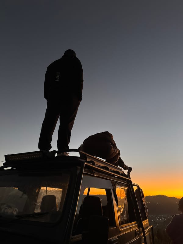 Two figures silhouetted on an SUV rooftop at dusk in Kintamani
