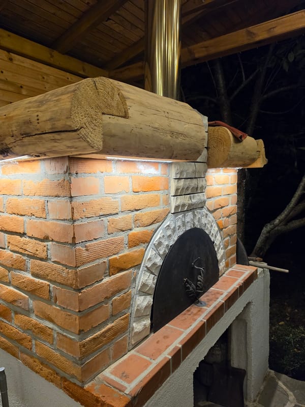 Rustic outdoor pizza oven space with string lights and greenery