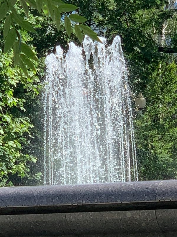 Pedestrians enjoy sunny afternoon at park fountain near Orthodox church