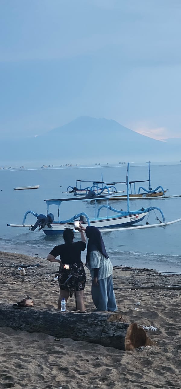 Two women observe ocean from Denpasar beach amid traditional boats