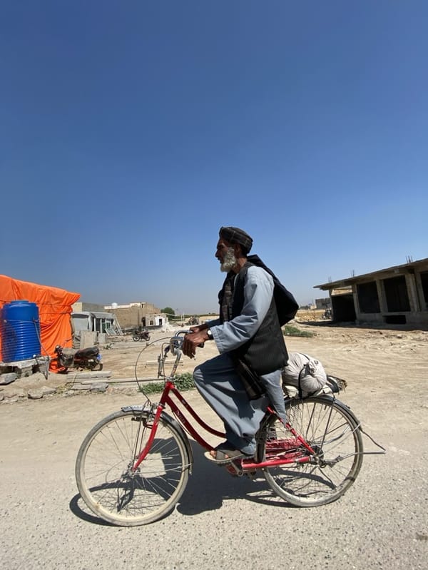 Man rides red bicycle on dirt road in Kandahar