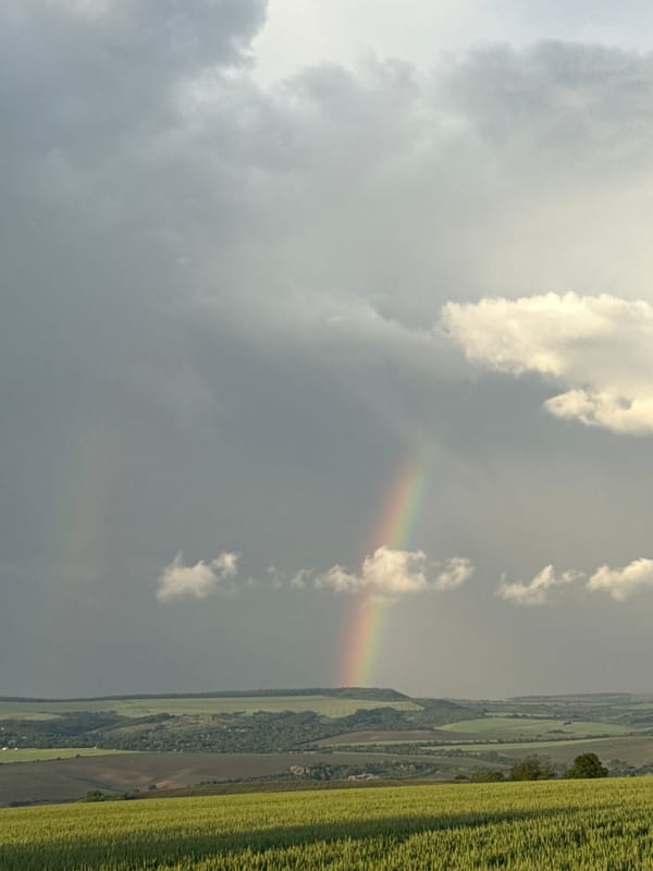 Rainbow appears through clouds over rural field landscape