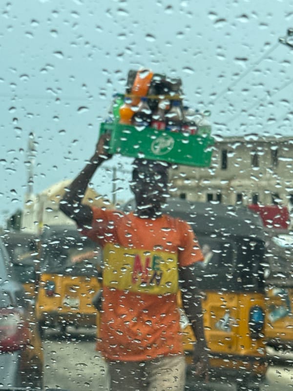 Street vendor carries bottles in basket during rain in Ado
