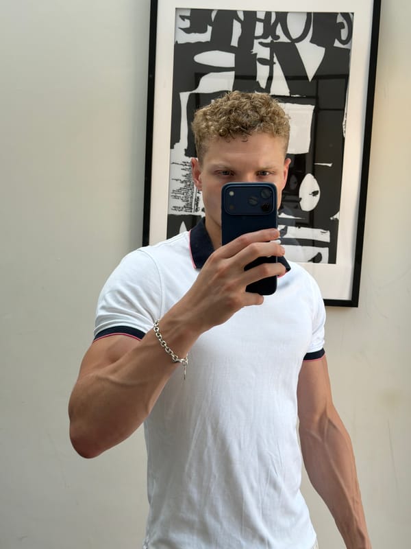 Mirror selfie in a London room, polo shirt and curly hair.