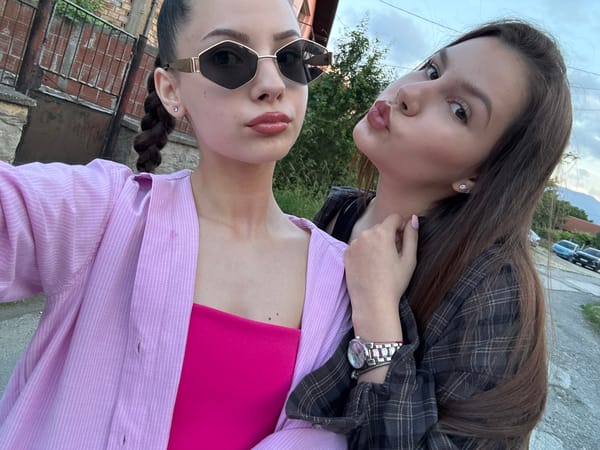 Two women photographed outdoors near residential street at dusk