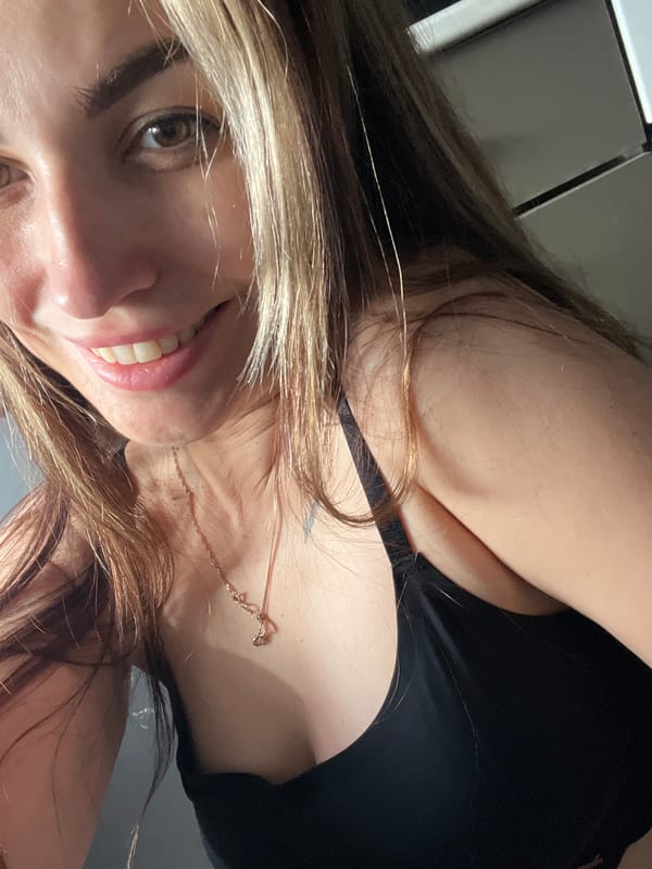 Woman takes selfies wearing black top and gold jewelry