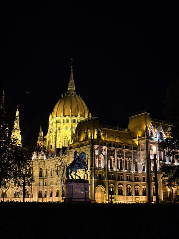 Tourists photograph illuminated Hungarian Parliament Building at night in Budapest