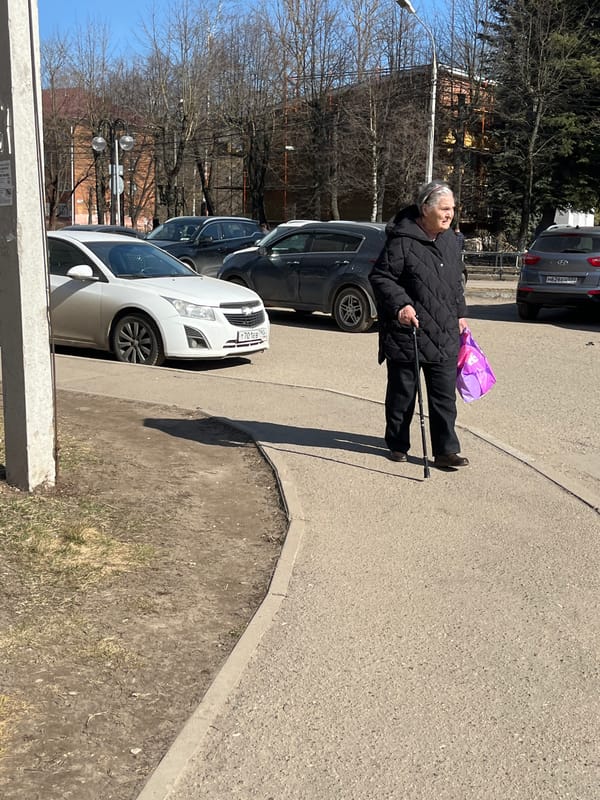 Elderly woman walks with cane on Klin sidewalk