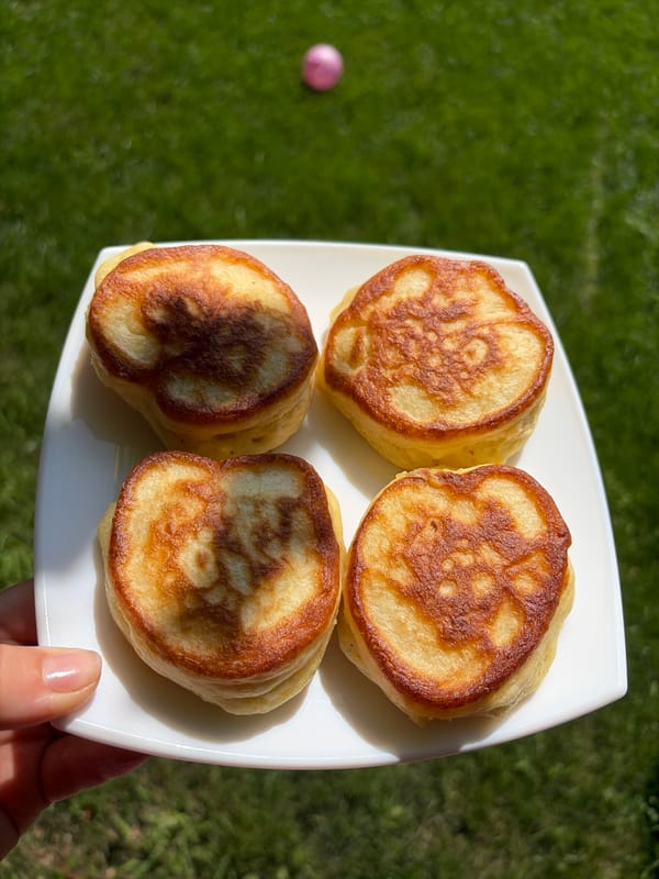 Thick golden pancakes on a white plate, held over green lawn