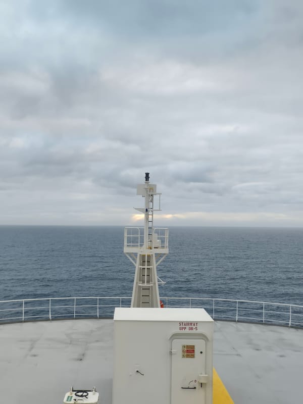 Choppy open sea from a ship's deck, overcast skies and a faint rainbow