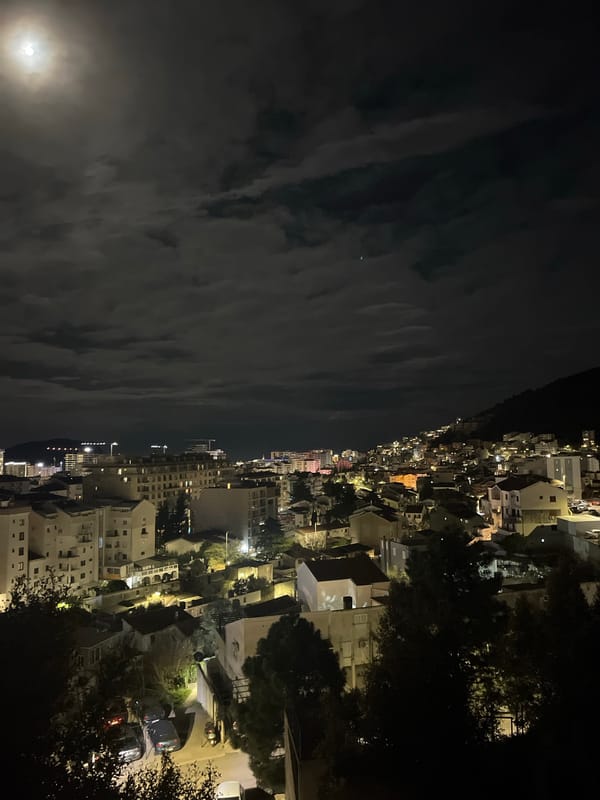 Moon visible over Budva cityscape on cloudy night