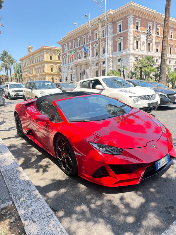 Red Lamborghini and Fiat Topolino parked on sunny Bari street