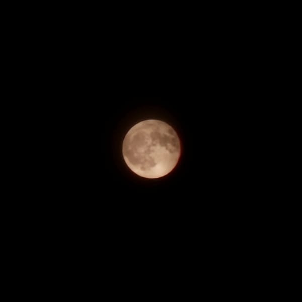 Reddish-orange moon rises through clouds over Basiano