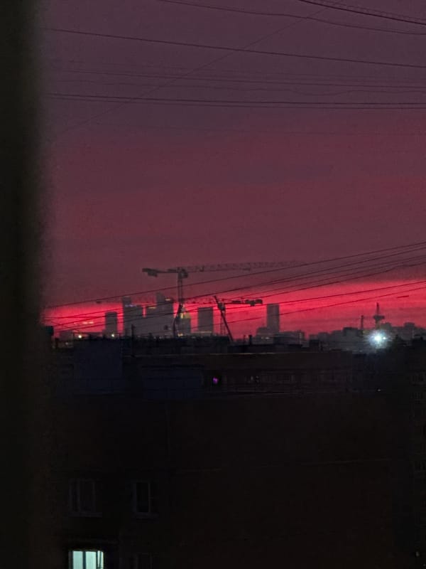 Red Sky Observed Over City With Construction Cranes