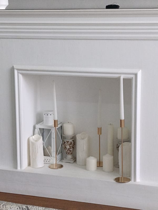 White mantelpiece styled with candles, lantern, and vase