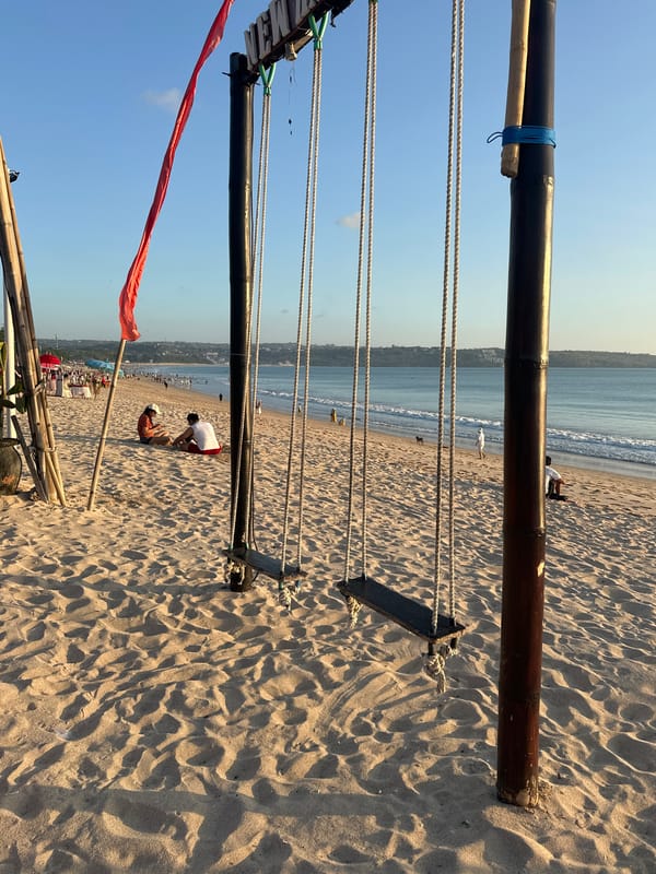 Kuta Beach at golden hour — swings, dining, and a calm sea