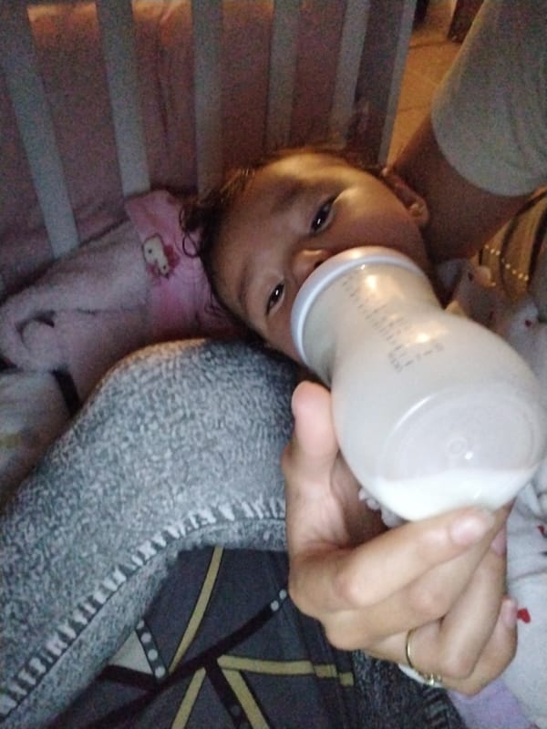 Baby bottle-feeds independently in crib with Hello Kitty blanket