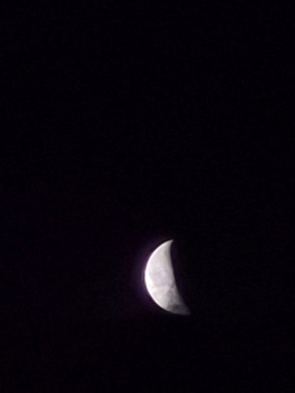 Crescent moon drifts through cloudy skies over rural Estonia