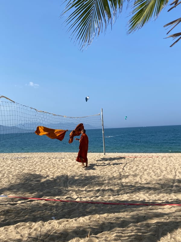 Nha Trang beach morning: kitesurfers, palm shadows, and a monk on the sand