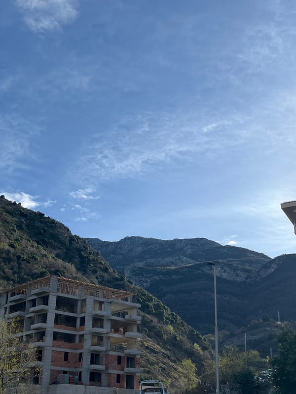 Woman holds real estate sign near Montenegro coastal buildings
