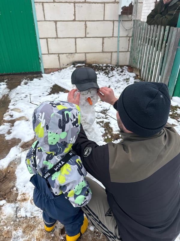 Father and child build snowman in Russian village yard