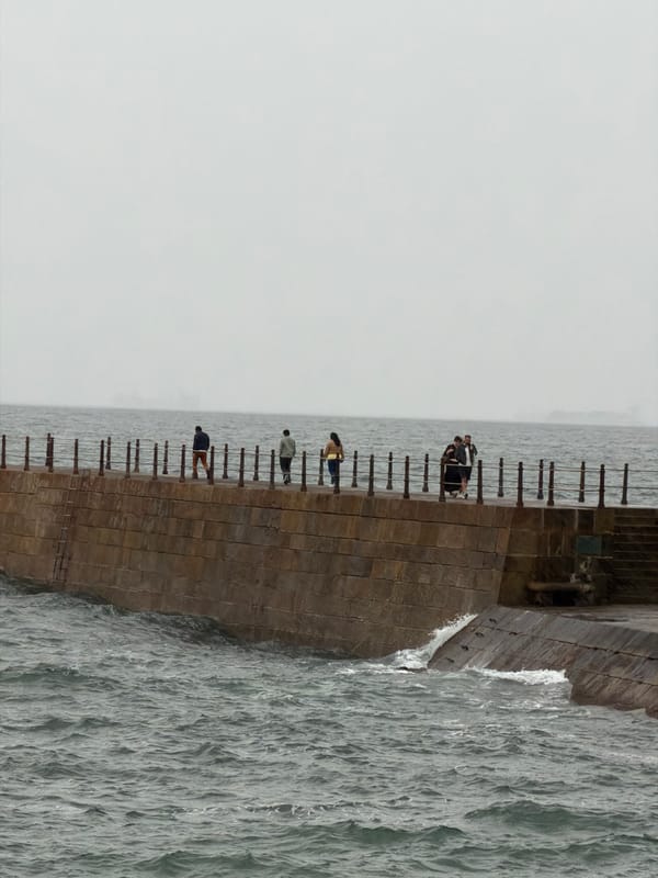 People gather on stone breakwater amid rough Atlantic seas
