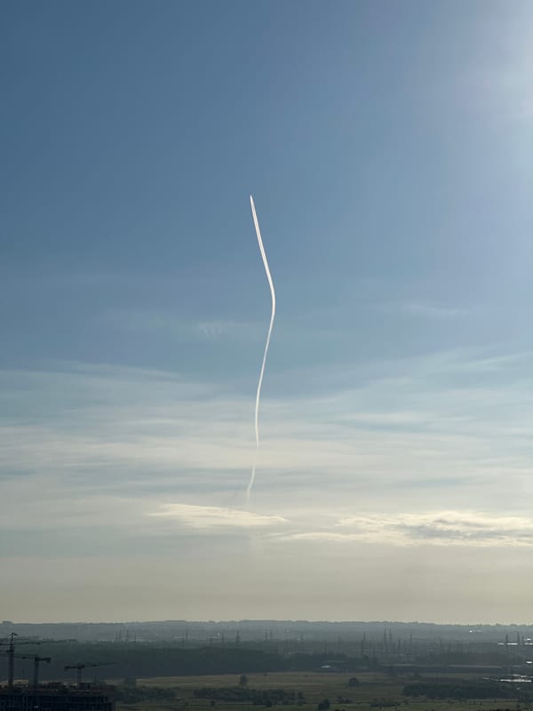 Contrail curves across a blue sky over Otradnoye