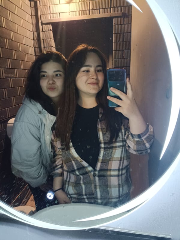 Two women take bathroom mirror selfie with decorative lighting