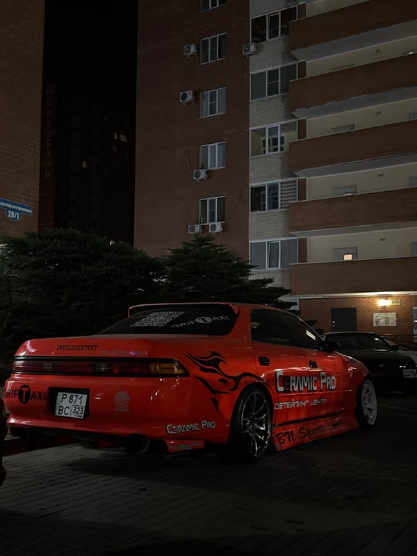 Modified drift car and neon signage on a brick-paved night street